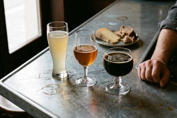 Trois bières de couleurs différentes servies au comptoir d'un bistrot, à côté d'une assiette